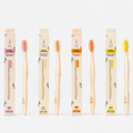 Four TANIT adult bamboo toothbrushes with packaging in orange, beige, pink and yellow